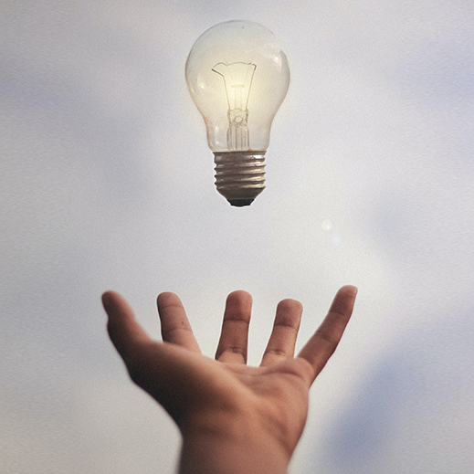 A hand reaching up towards a glowing lightbulb